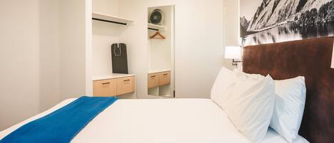A hotel room with a neatly made bed, a wooden nightstand, a dresser, and a mirror.