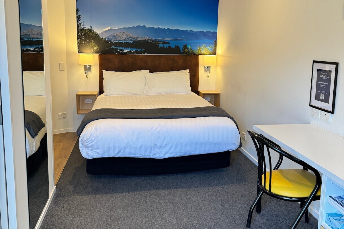 Una habitación de hotel con una cama, un escritorio, una silla y un gran mural en la pared.