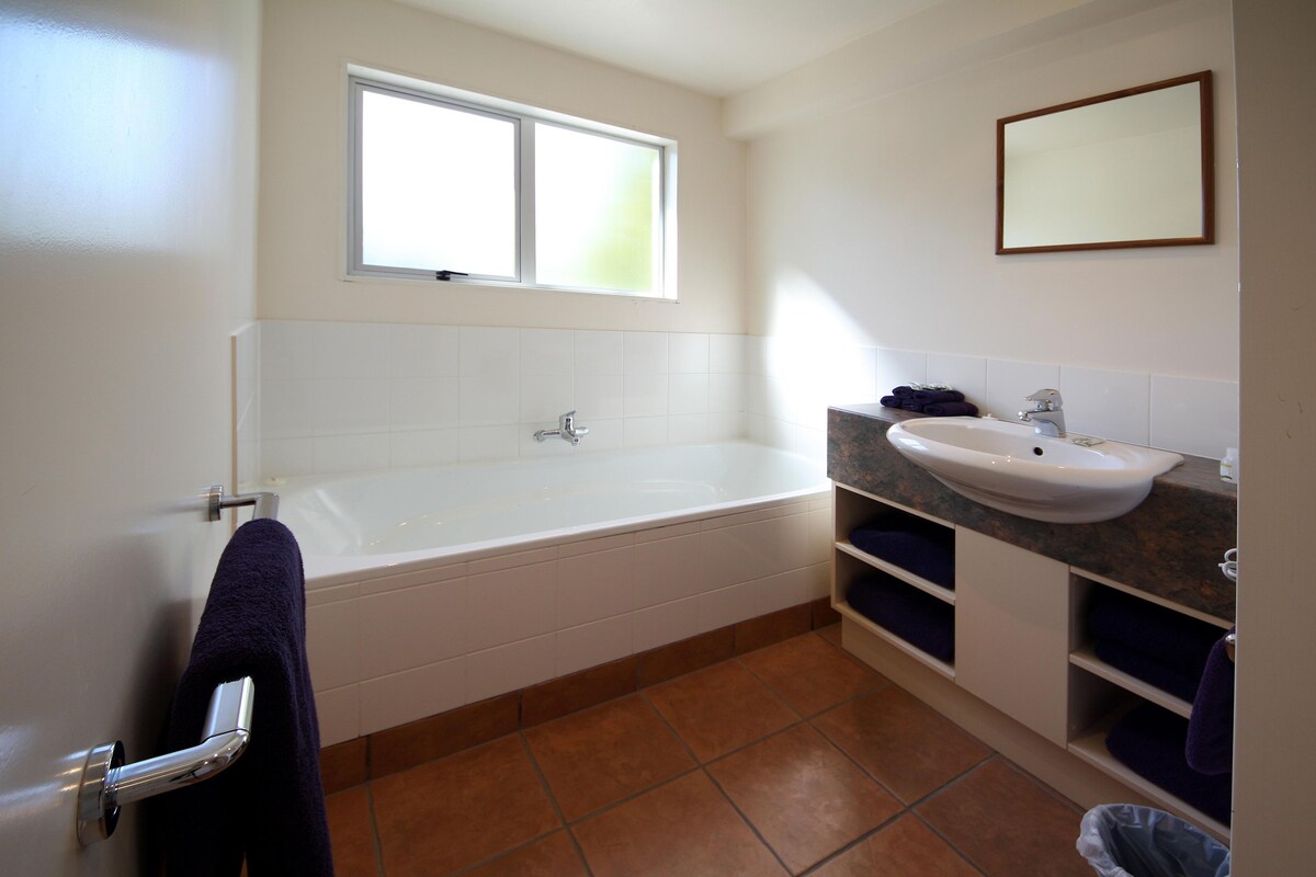A bathroom with a bathtub, a sink, a window, and a mirror.