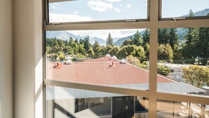 A view from a window overlooking a mountainous landscape with trees and a building with a red roof. - Blue Peaks Lodge (Queenstown)