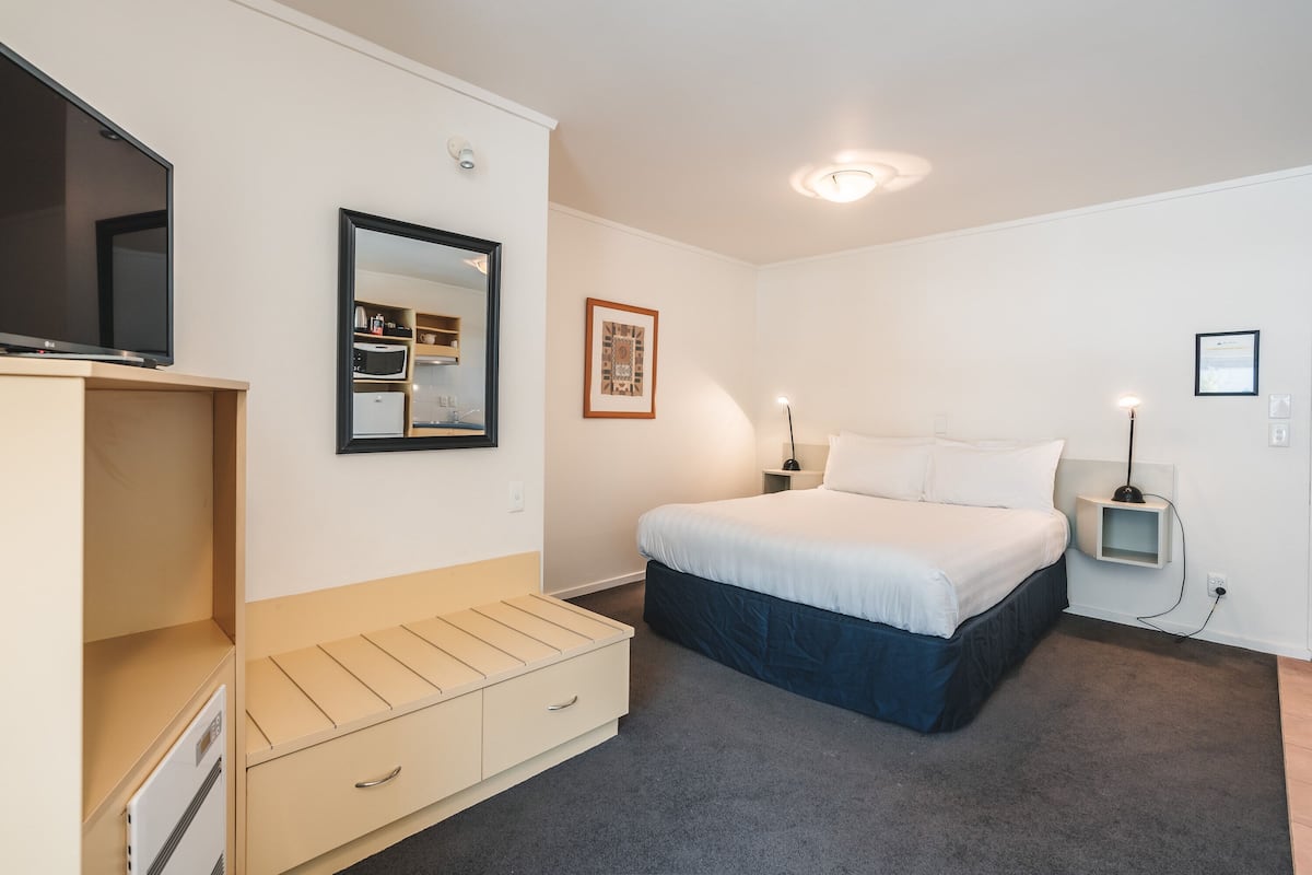 Un dormitorio con cama, televisión, cómoda, espejo y mesita de noche con lámpara.