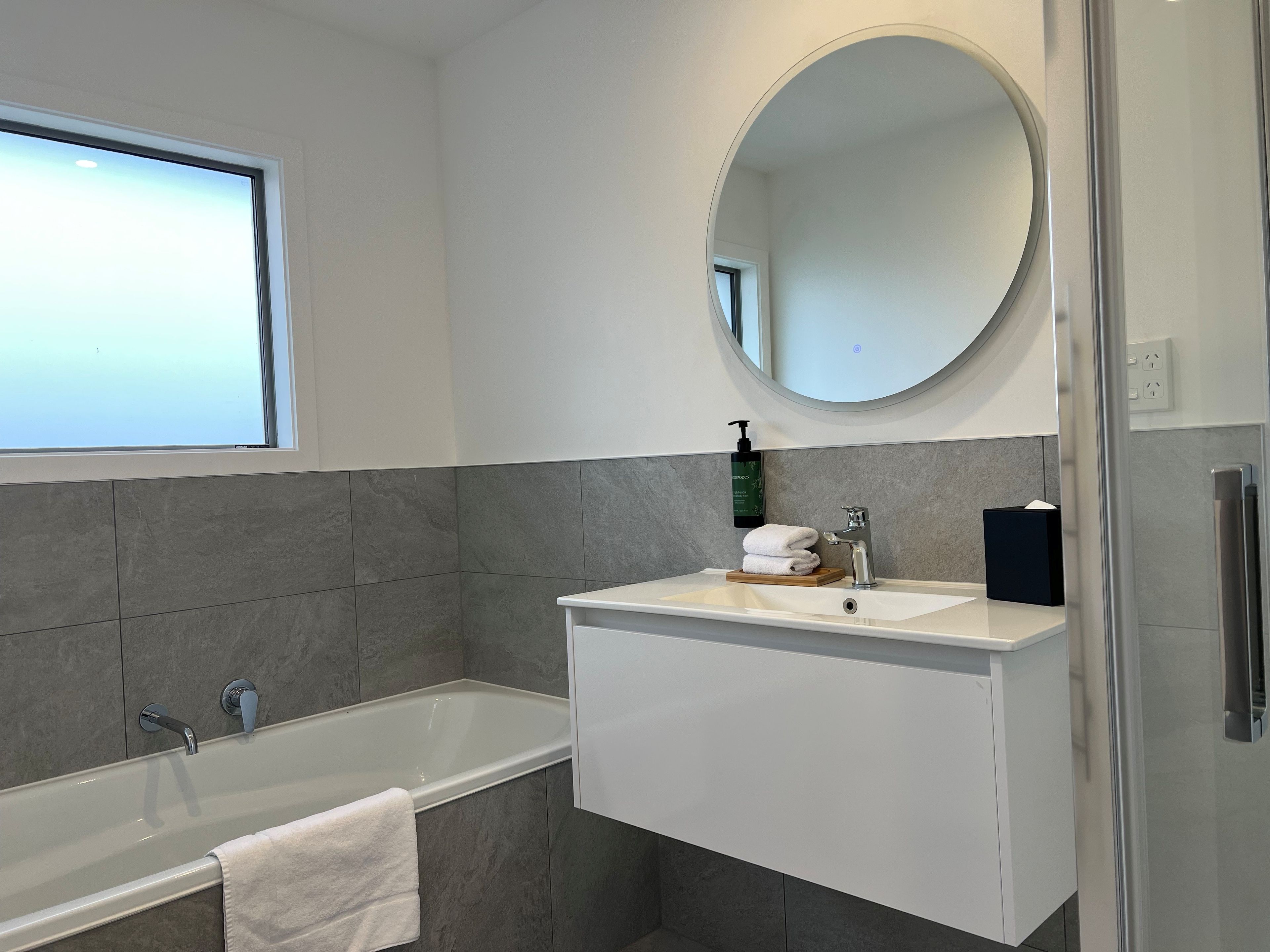 A modern bathroom with a bathtub, a sink with a mirror above, and a window.