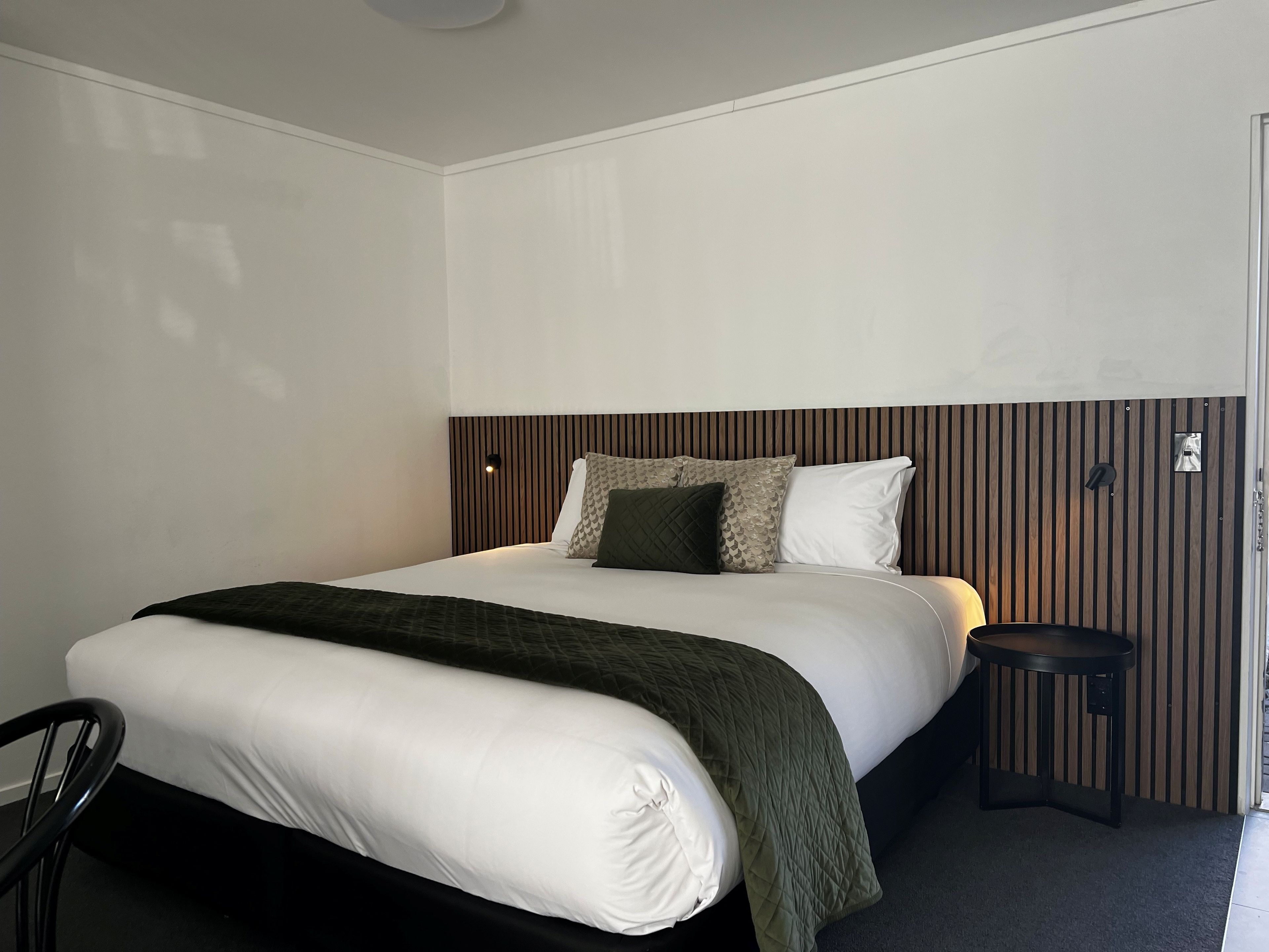 A hotel room with a bed, a bedside table, and a chair.
