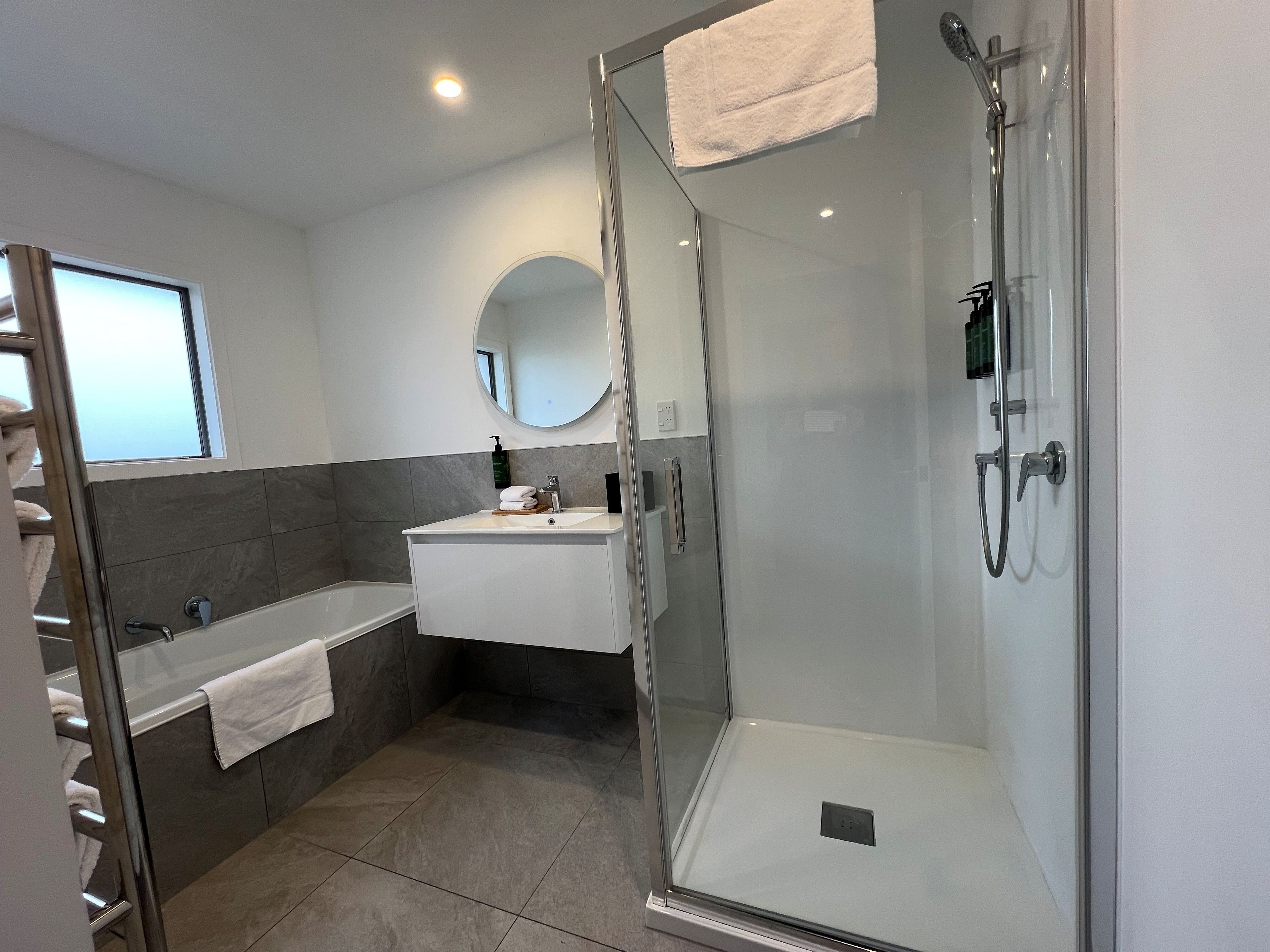 Un baño moderno con ducha envuelta en vidrio, un lavabo blanco y un espejo sobre él.