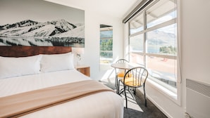 A hotel room with a large bed, a chair, a table, and a view of mountains through the window. - Blue Peaks Lodge (Queenstown)