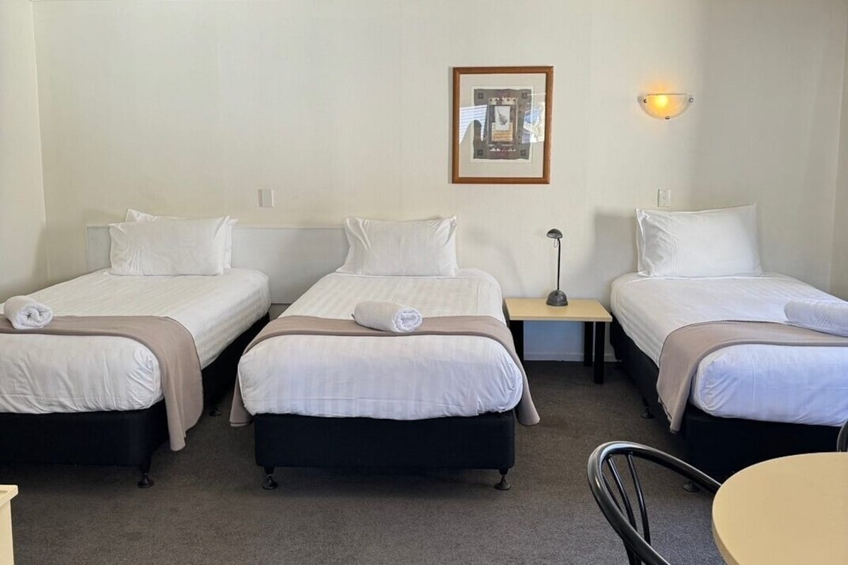 Habitación de hotel con tres camas individuales, una mesita y una silla.