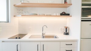 A modern kitchen with white cabinetry, a stainless steel sink, and wooden shelves above. - Blue Peaks Lodge (Queenstown)