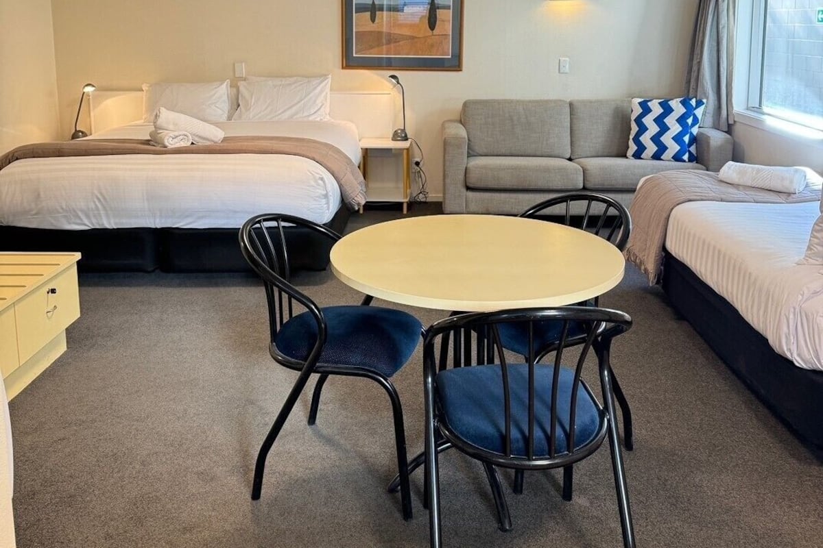Habitación de hotel con cama, sofá, mesa y sillas, lámpara y un cuadro en la pared.