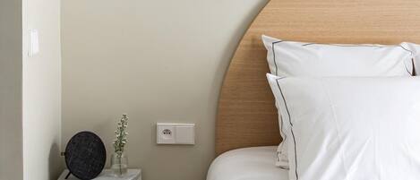 Un dormitorio ordenado con una mesita de noche curva, una lámpara de pared y una cama con ropa de cama blanca.