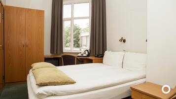 Ein Hotelzimmer mit Bett, Schreibtisch, Stuhl, Kleiderschrank und einem Fenster mit Vorhängen.