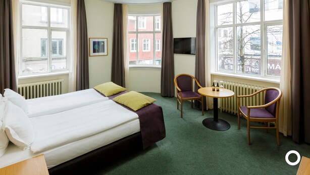 Une chambre d’hôtel avec un lit, deux chaises, une petite table et un téléviseur.
