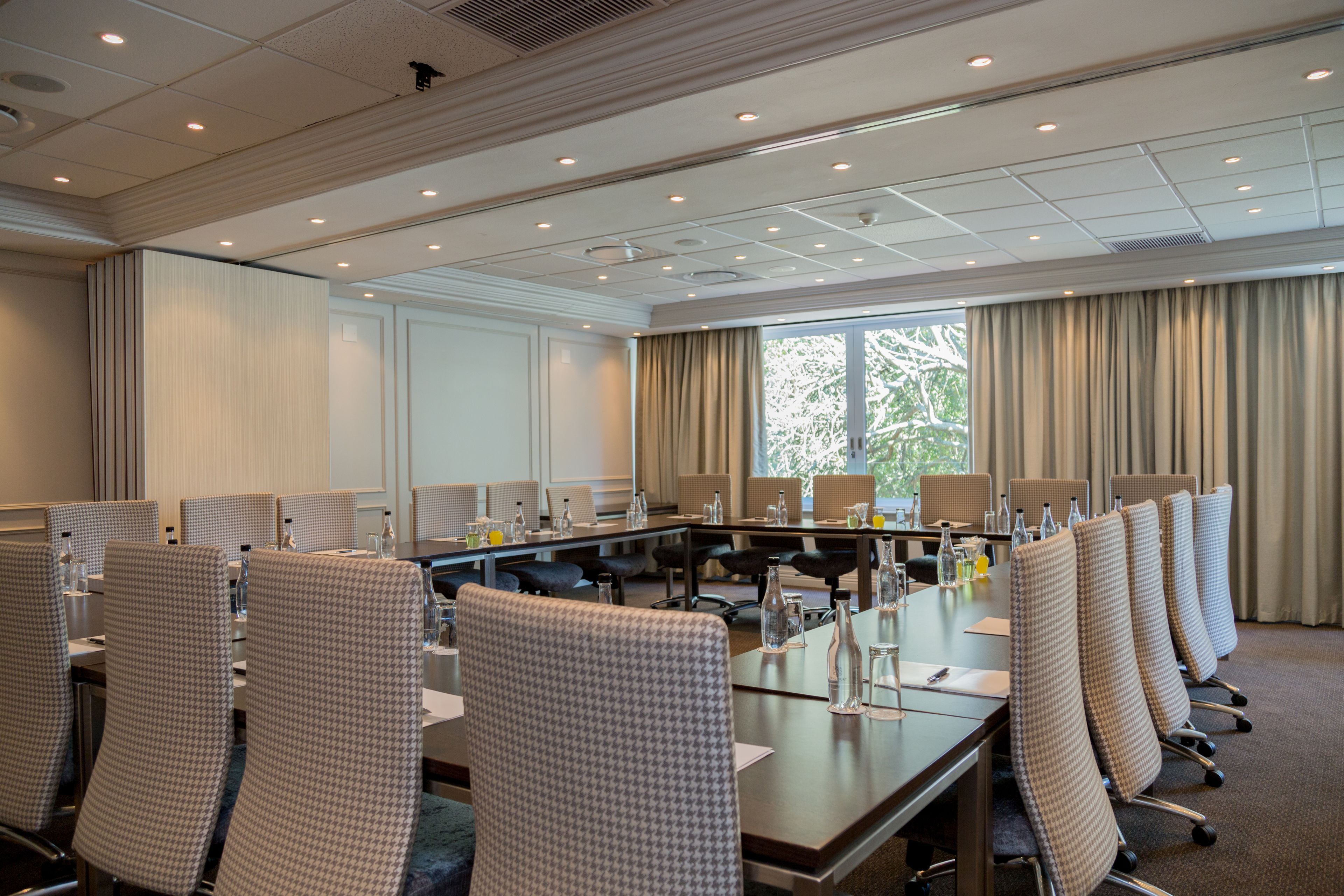 A conference room with a long table, multiple chairs, and a view of trees through large windows.