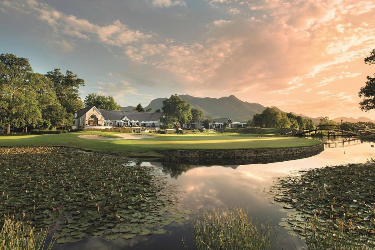 A golf course with a pond in the foreground, surrounded by trees and a mountain in the background.