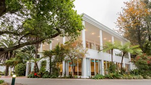 A modern building with a white facade, large windows, and a landscaped garden with various plants and trees.