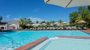 A swimming pool with lounge chairs and umbrellas, surrounded by palm trees and a clear blue sky.