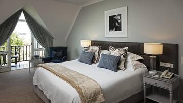 A bedroom with a large bed, two bedside lamps, a framed picture on the wall, and a balcony with a chair and table.