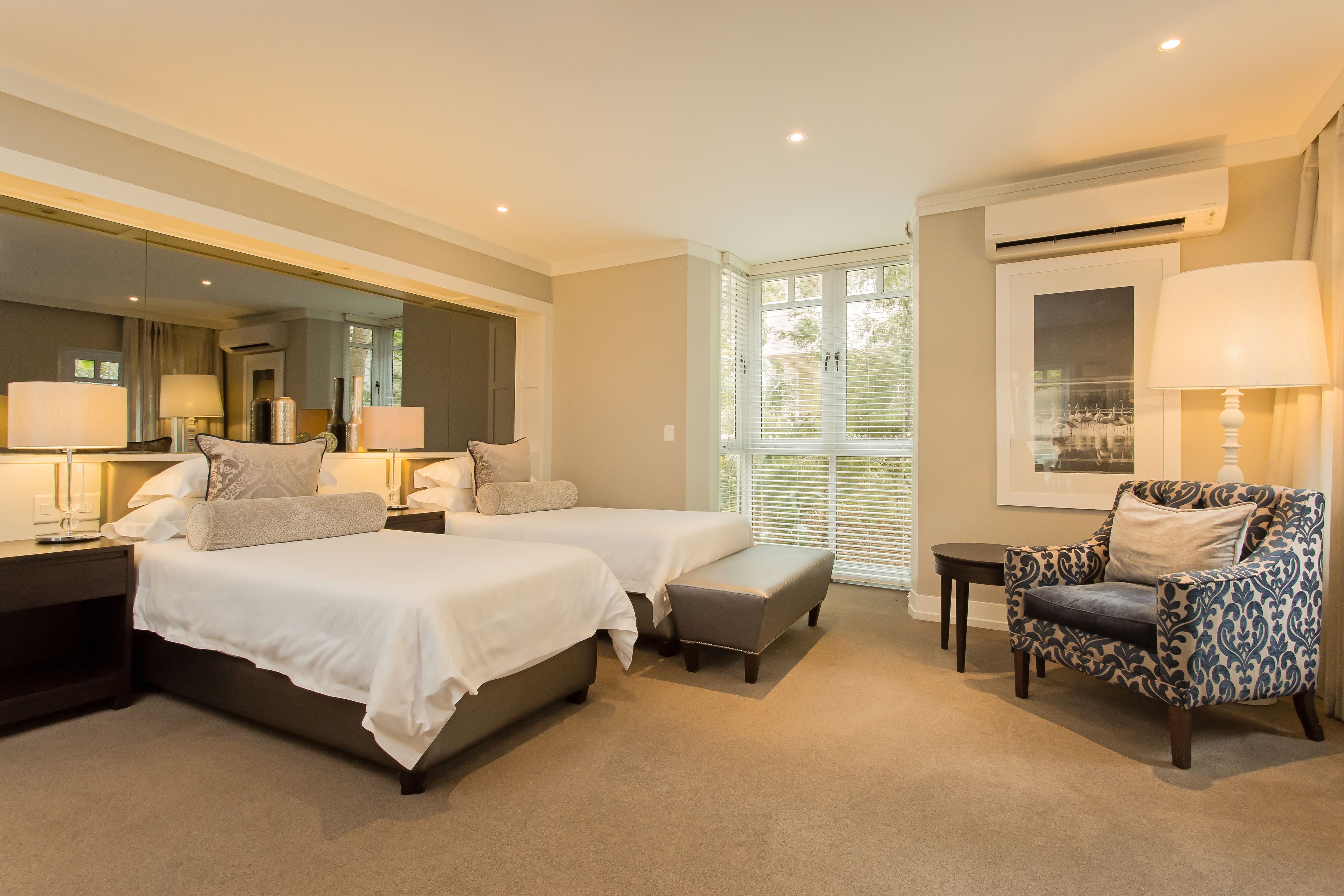 A bedroom with two beds, a chair, a nightstand, and a window with blinds.