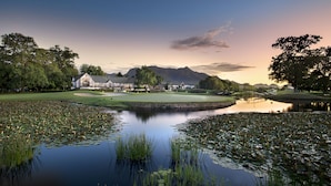 A golf course with a pond, trees, and a building in the background.