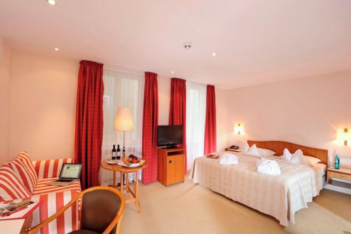 A hotel room with a bed, a sofa, a TV, and a desk with a lamp.
