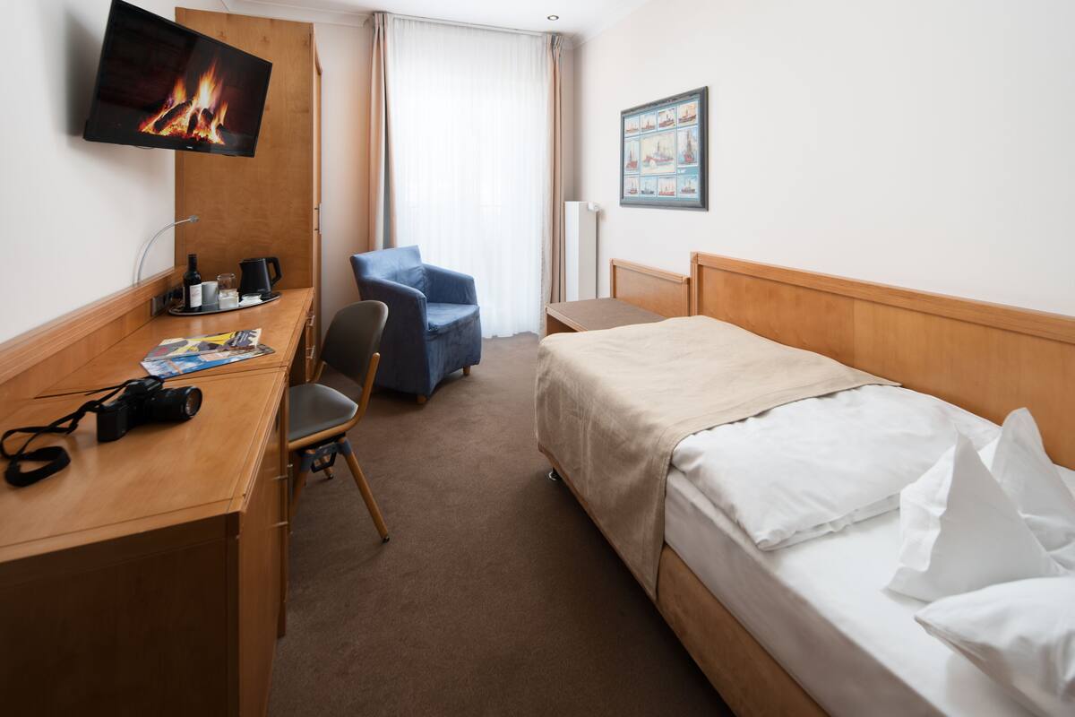 A hotel room with a bed, a desk with a chair, a television, and a window with curtains.