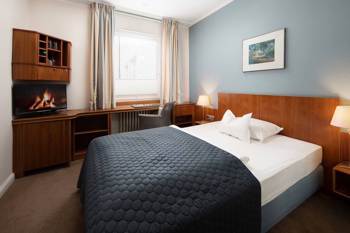 A hotel room with a bed, a desk, a television, and a window with curtains.