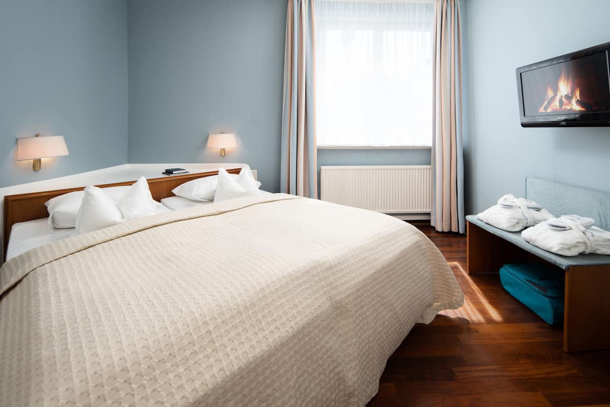 A hotel room with a large bed, two bedside lamps, a television, and a bench with towels.