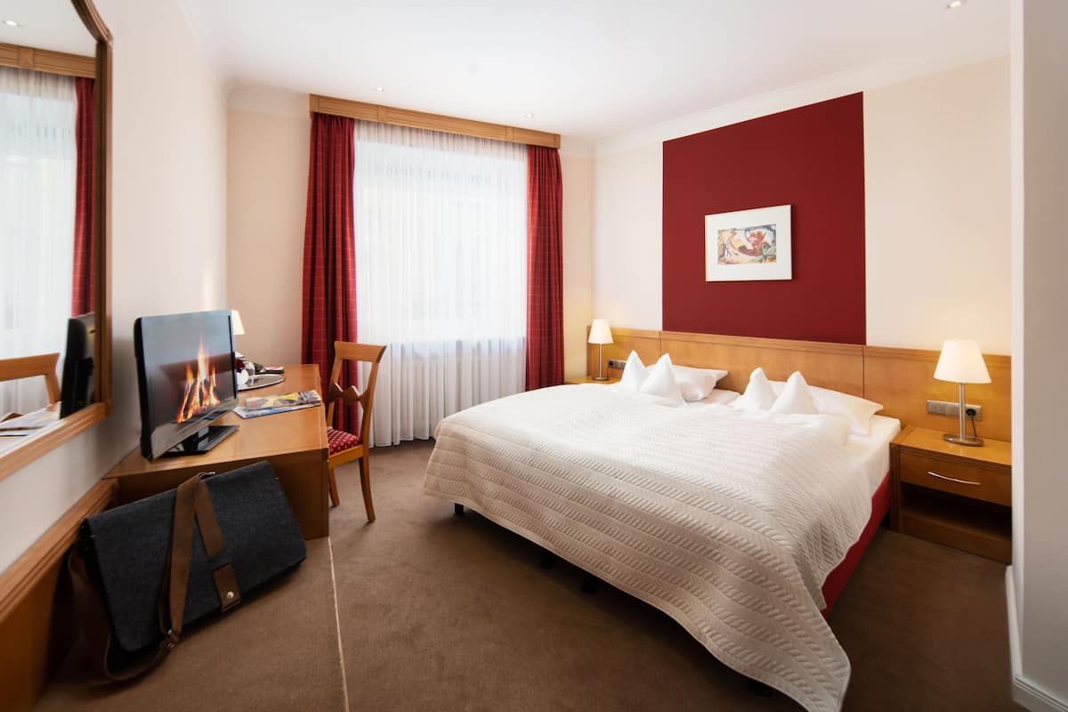 A hotel room with a large bed, a desk with a computer, a chair, and a TV.