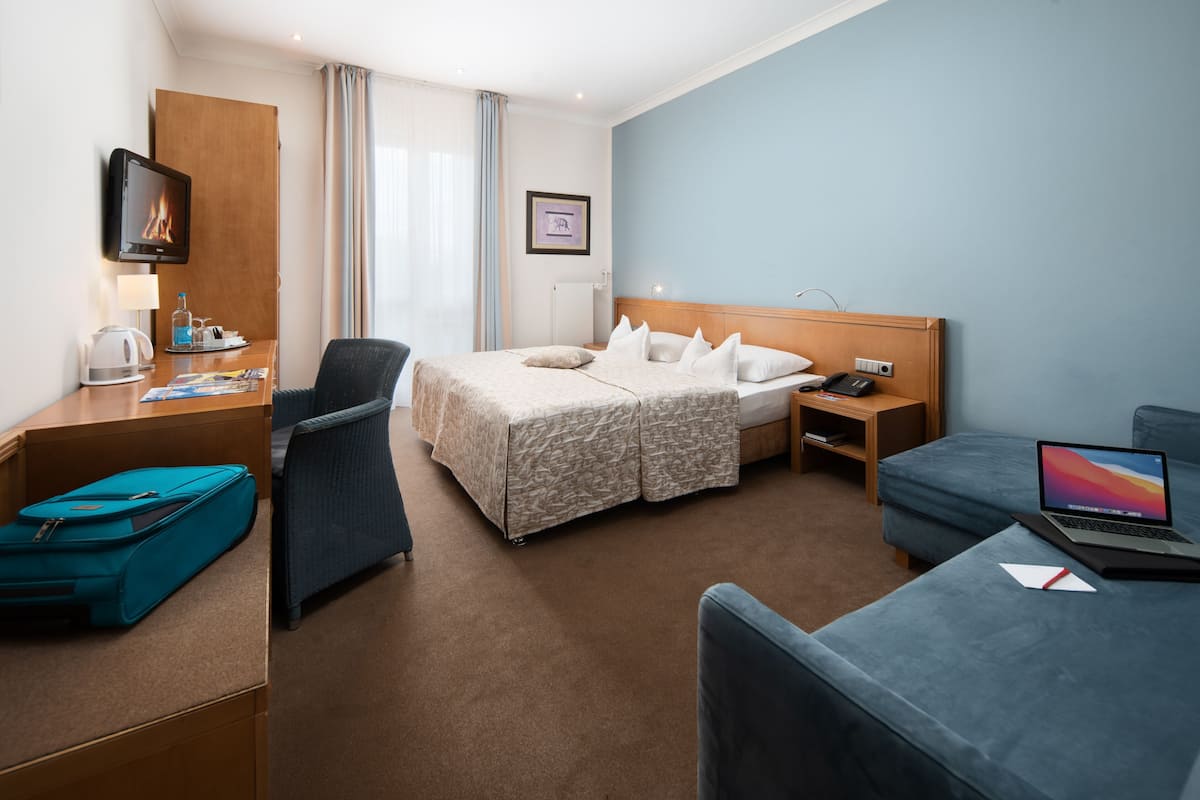 A hotel room with a bed, desk, chair, and a laptop on a small couch.