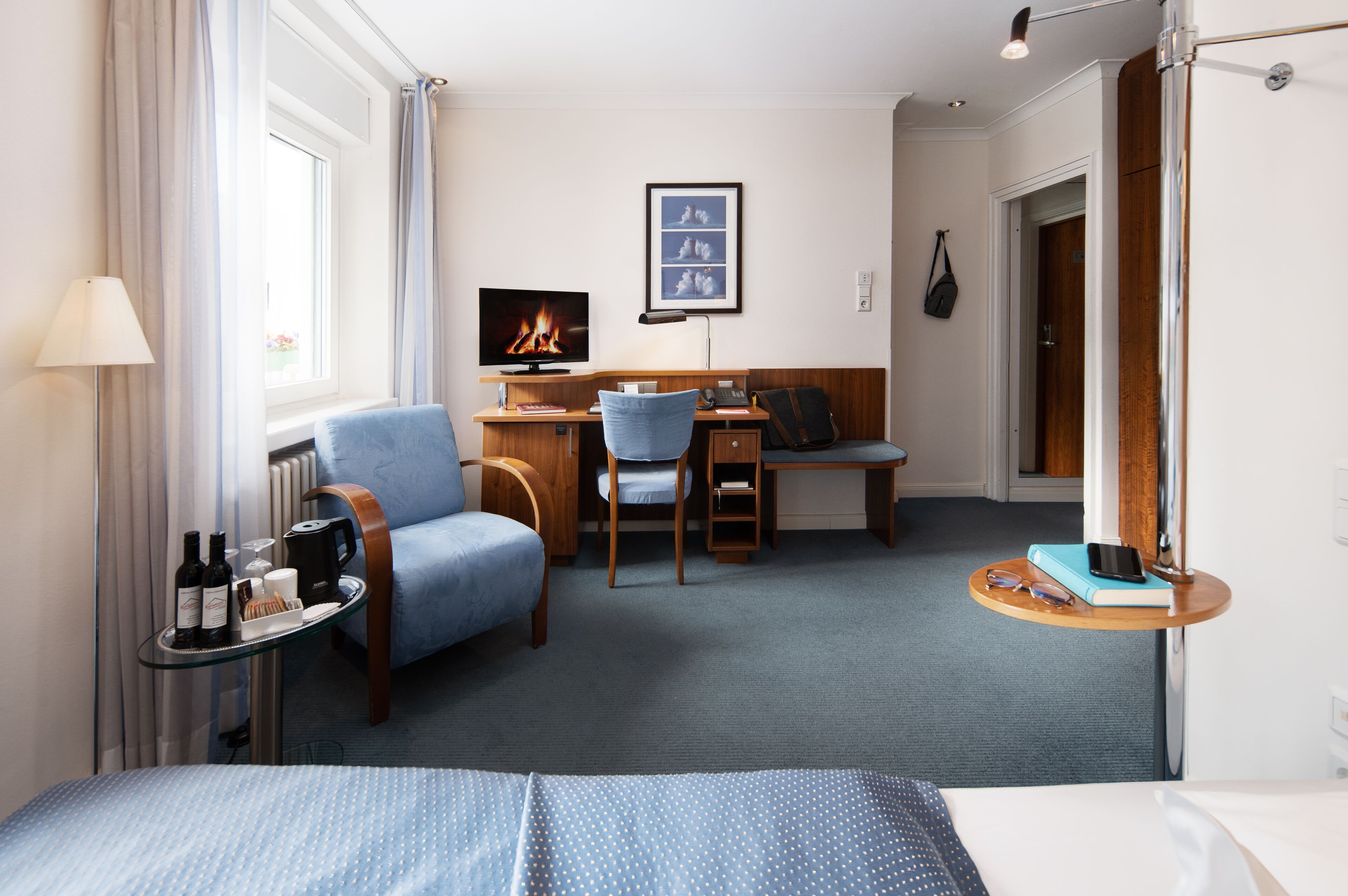Habitación de hotel con cama, escritorio, silla, pequeña mesa con lámpara, televisor y chimenea.