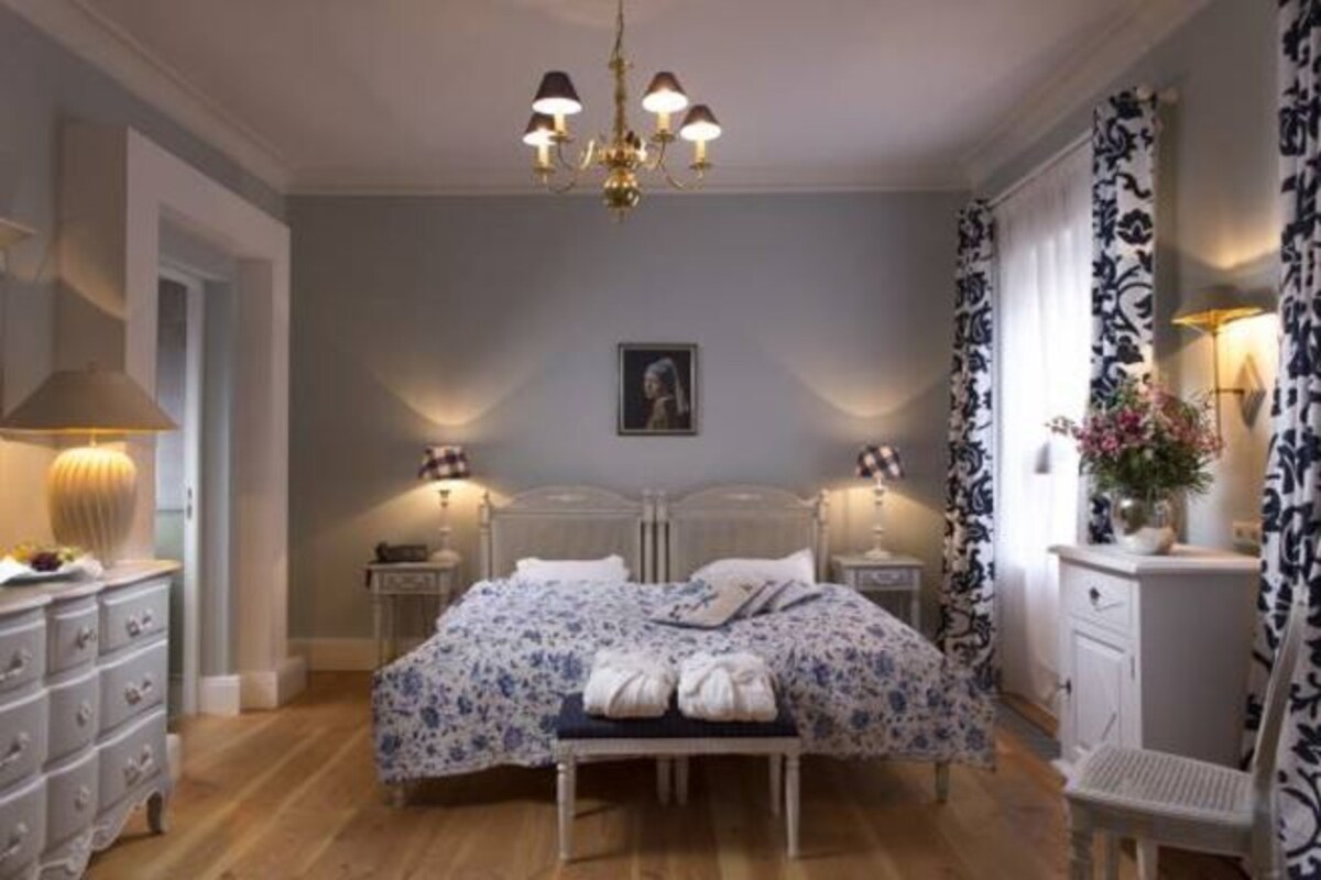 A bedroom with a double bed, bedside tables, a bench, a dresser, and a chandelier.