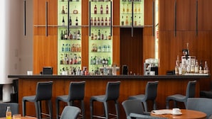A bar area with wooden paneling, multiple shelves of liquor bottles, and bar stools. - Hotel Baseler Hof (Hamburg)