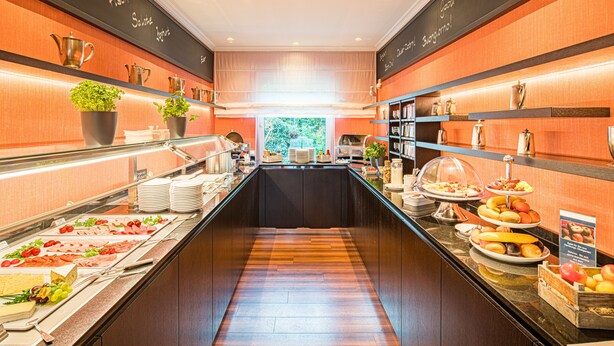 A buffet area with various food items, including fruits, cheeses, and meats, arranged on glass shelves and counters. - Hotel Central (Hamburg)
