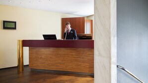 A reception desk with a wooden finish, a digital display, and a person standing behind it. - Hotel Central (Hamburg)