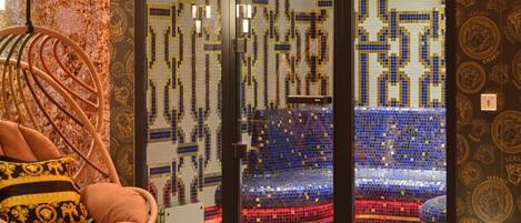 A room with a mosaic wall, a hanging chair with a patterned cushion, and a view of a stadium through a glass door.