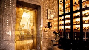 Un hall d’entrée luxueux avec un sol en marbre, une porte d’entrée en verre, un meuble à vin et une petite table surmontée d’un vase.