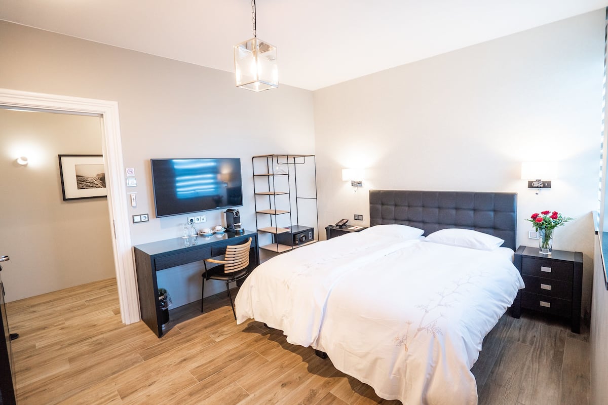 Ein modernes Schlafzimmer mit einem großen Bett, einem Schreibtisch mit Computer, einem Stuhl und einem Fernseher.