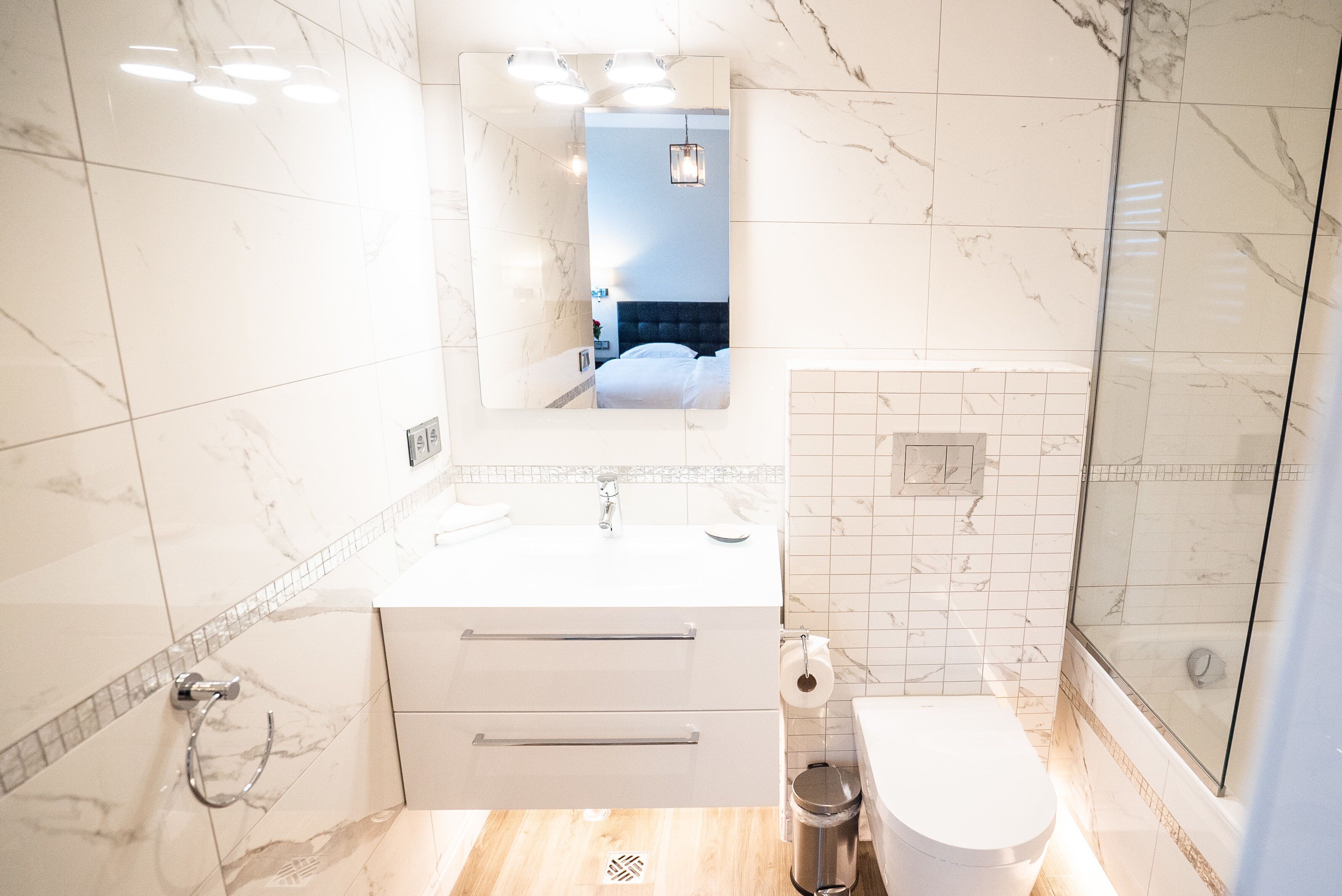 A modern bathroom with a marble floor, a white sink, a mirror, and a glass shower enclosure.
