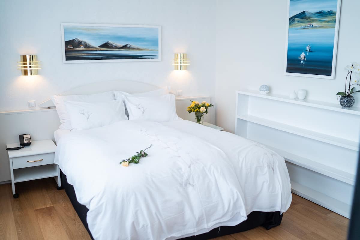 Ein ordentlich eingerichtetes Schlafzimmer mit einem weißen Bett, Nachttischen und Wandbildern.