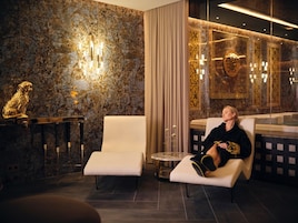 A luxurious hotel lobby with marble walls, a gold statue, and a seating area with a massage chair.