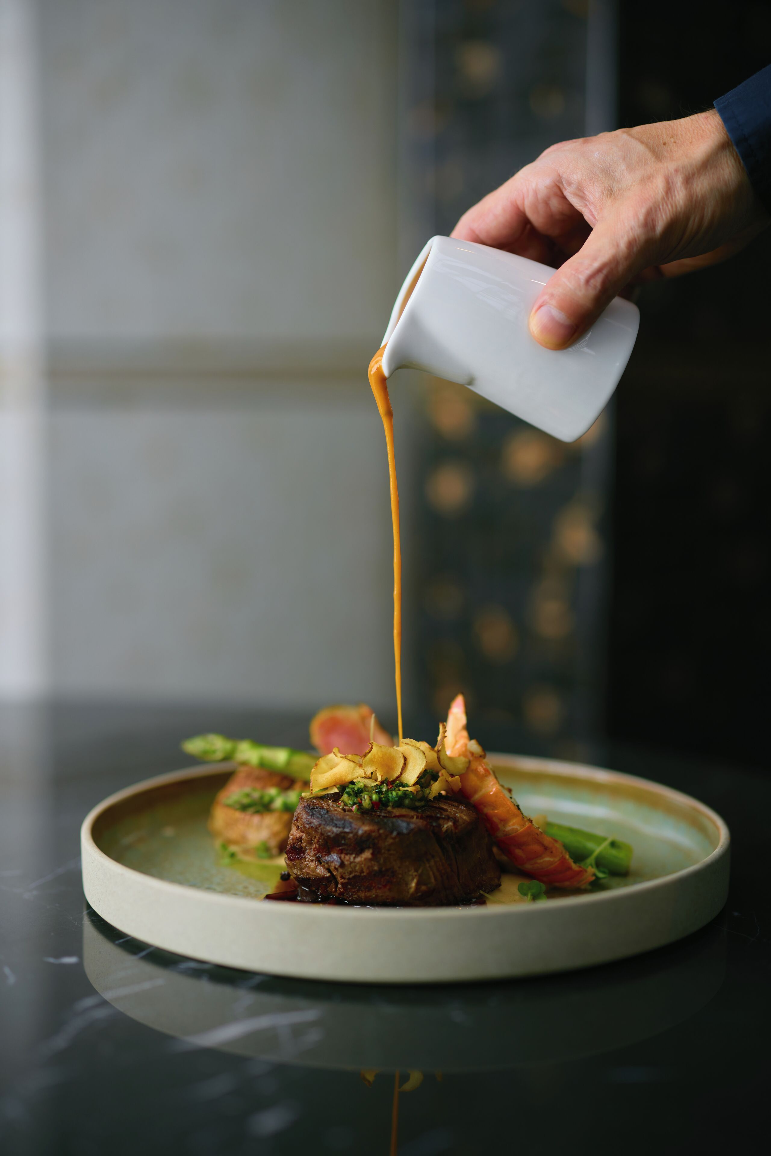 A hand pouring sauce over a dish of food.