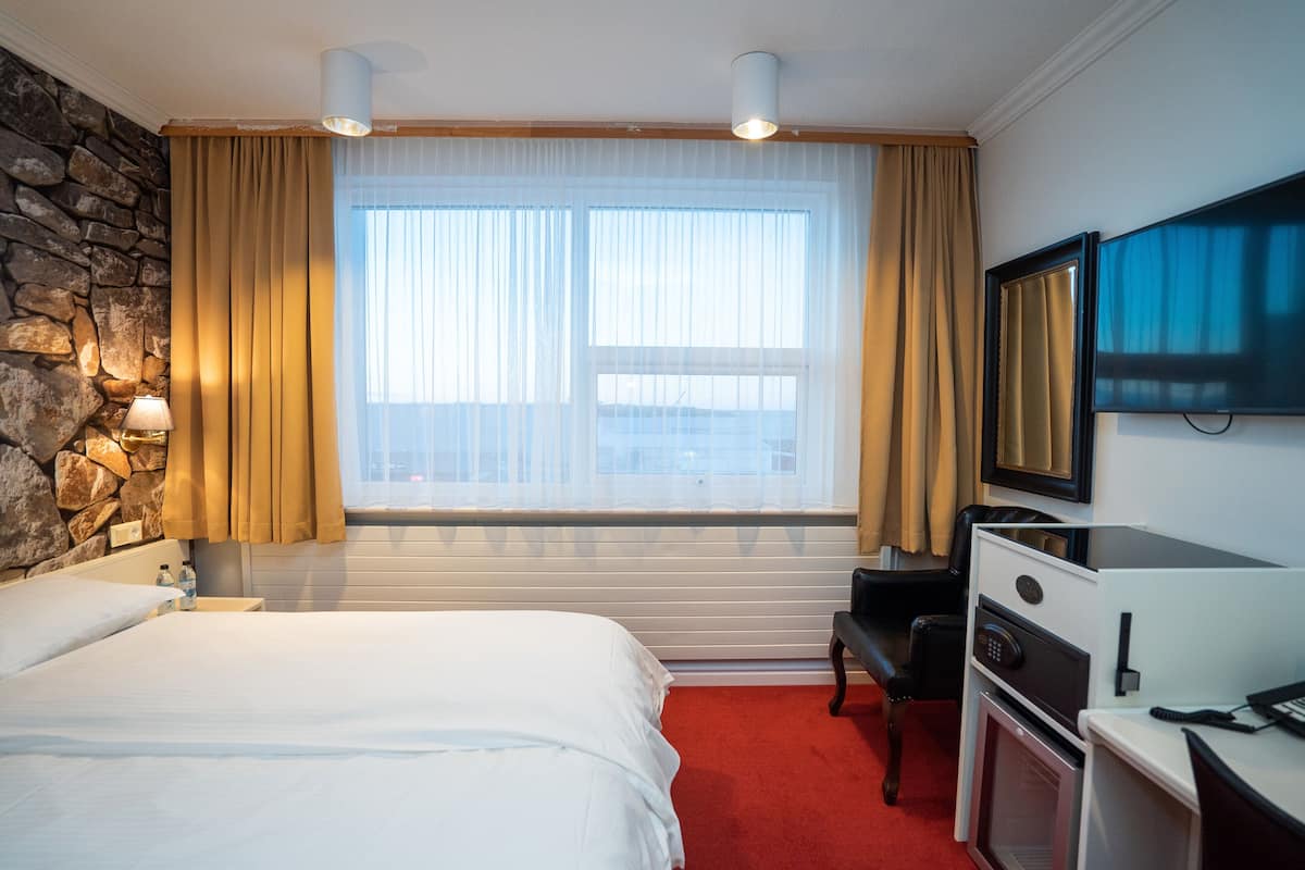 Ein Hotelzimmer mit Bett, Schreibtisch, Fernseher, einer Steinsäule und einem Fenster mit Vorhängen.