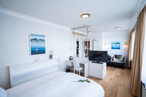 Habitación de hotel con cama, escritorio, televisión y vista al mar.
