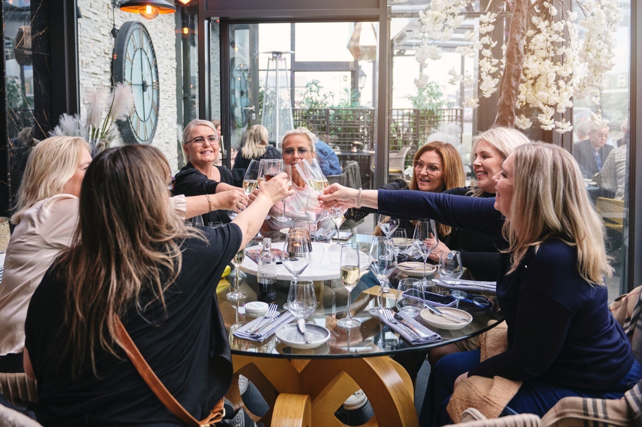 A group of people toasting at a round table with wine glasses, surrounded by neatly arranged plates and cutlery.