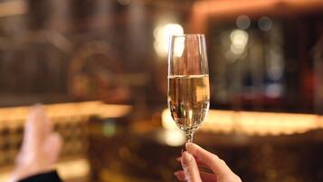 A person holding a champagne glass, reclining on a white sofa in a dimly lit room with a bar in the background.