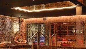 Un espace spa moderne doté d’un bain à remous aux motifs de mosaïque, de sièges agrémentés de coussins et offrant une vue sur le paysage urbain à travers un mur de verre.