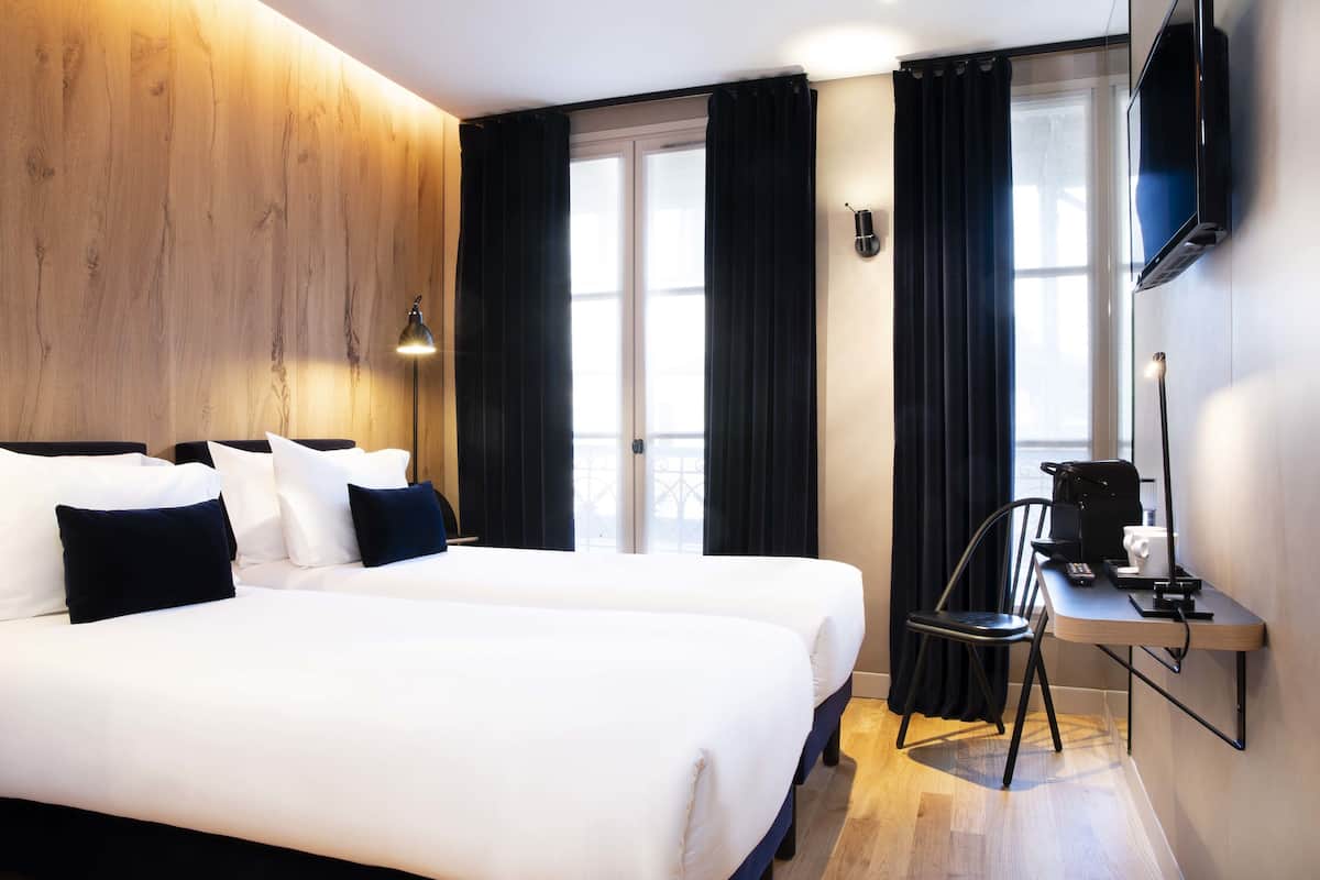 Een hotelkamer met twee bedden, een bureau met stoel, een televisie en een raam met gordijnen.
