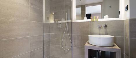 Un baño moderno con ducha de vidrio, lavamanos integrado y espejo sobre el mueble.