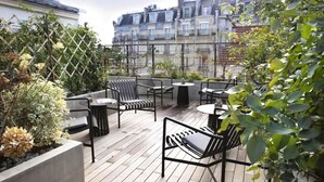 Une terrasse sur le toit, aménagée avec des espaces de détente en plein air, comprenant des chaises et des tables, entourée de verdure et offrant une vue sur le paysage urbain.