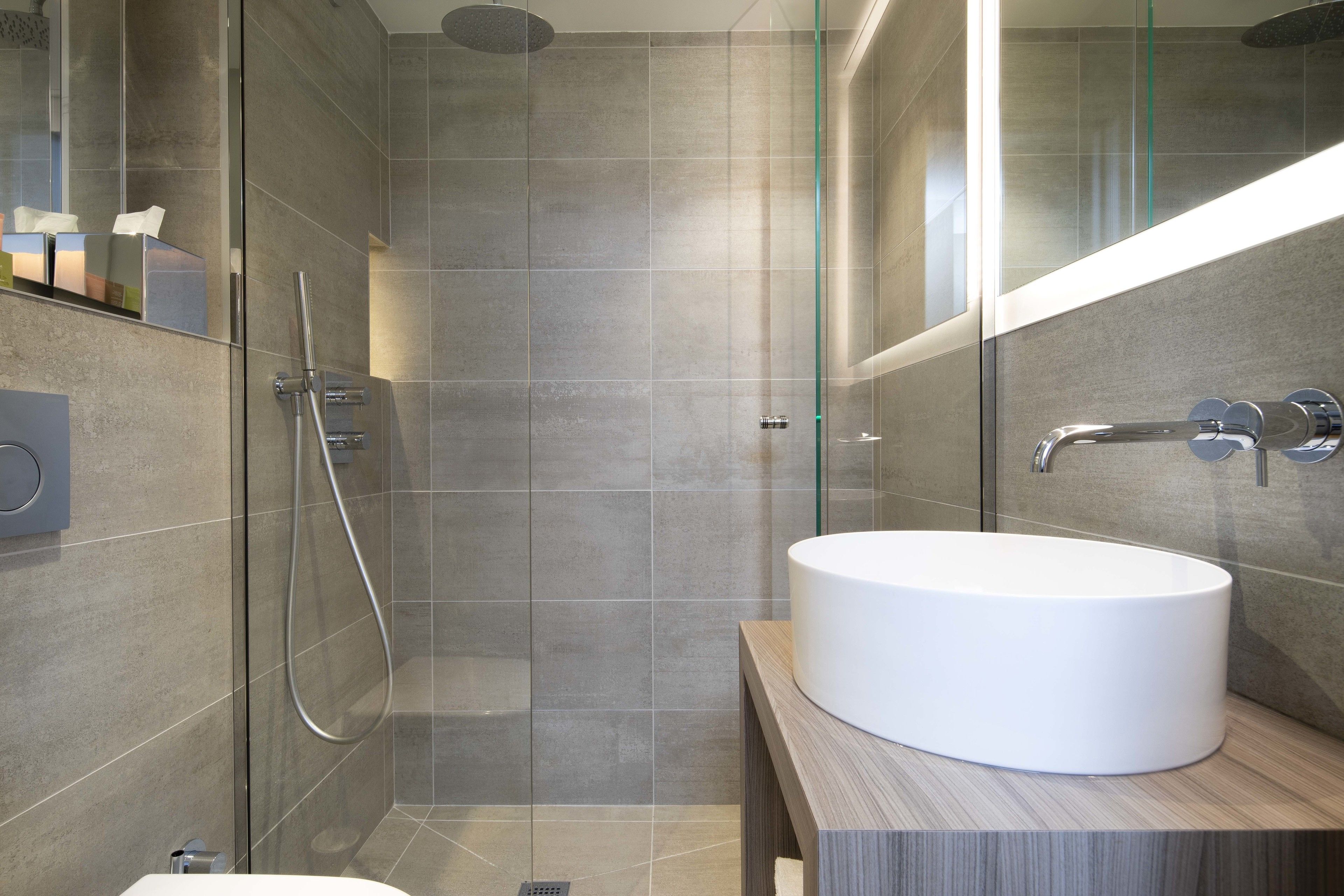 A modern bathroom with a glass-enclosed shower, a white sink, and a wooden vanity.