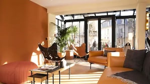 Un salon moderne avec un canapé, des fauteuils et une table basse. Une grande fenêtre offre une vue sur la ville.